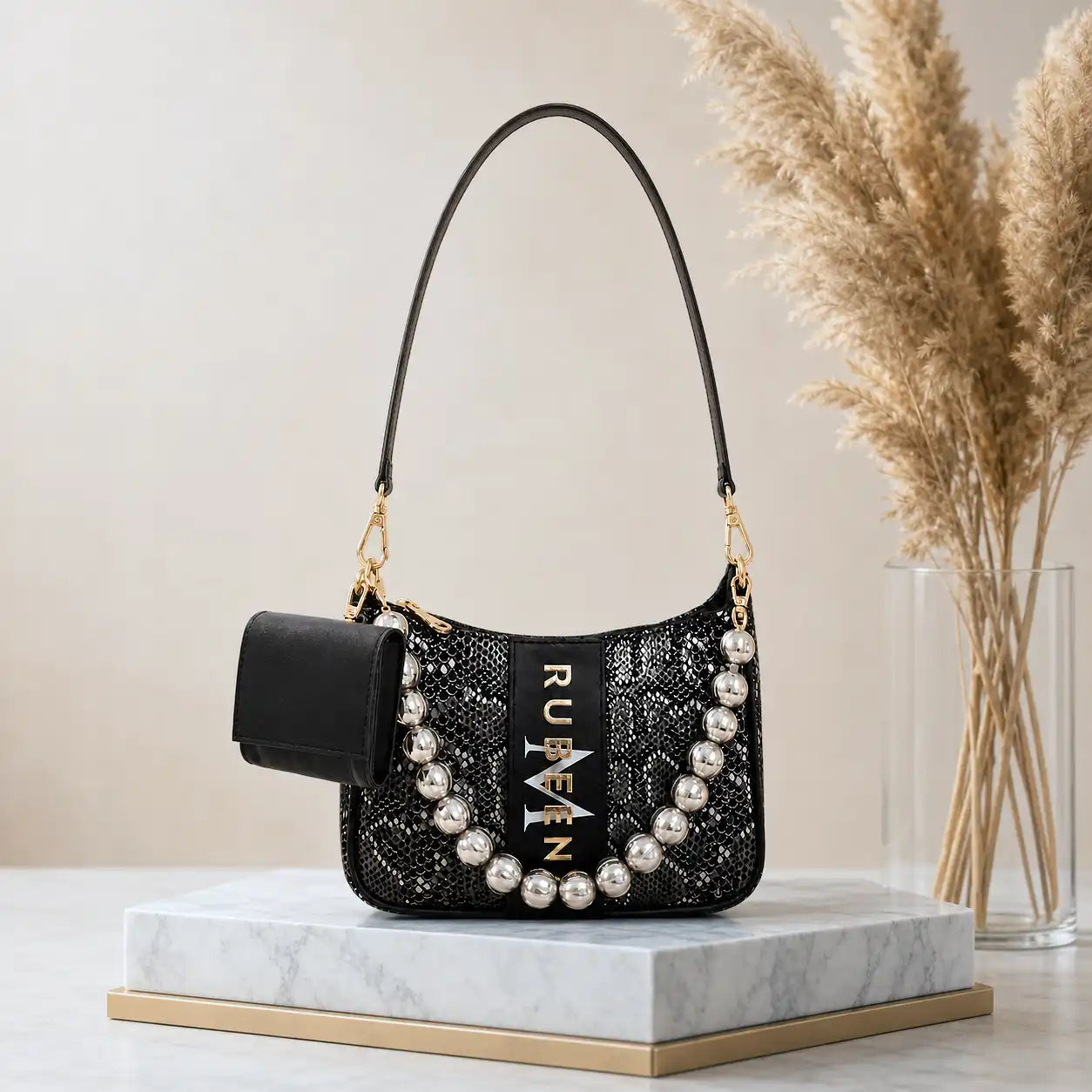 Black personalized sling bag by TPC Gifts with pearl embellishments on a marble surface with decorative elements.