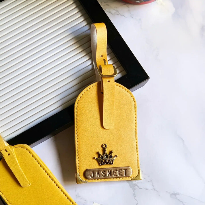 A yellow faux-leather luggage tag with a crown emblem and a metal plate engraved with &