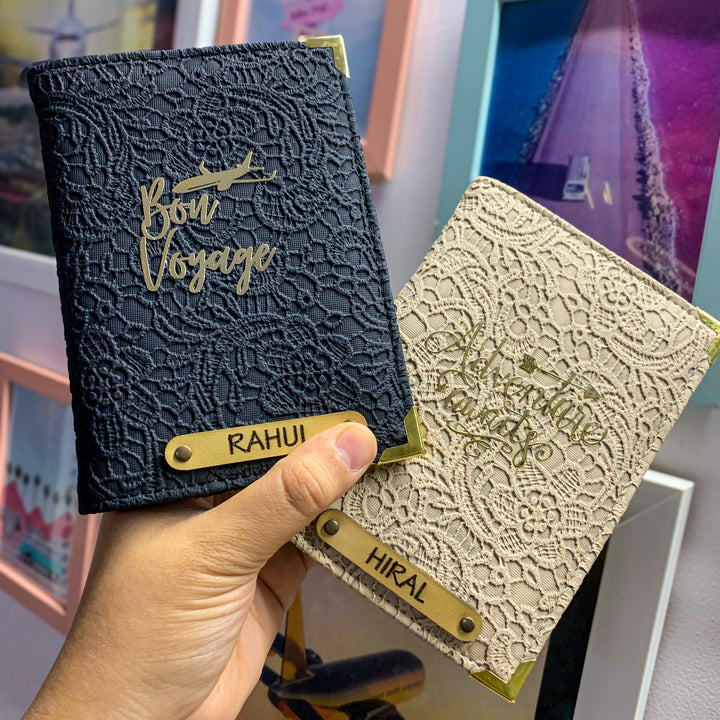 Two people holding black and white couple passport covers with custom text and charms, displayed in an airport setting.