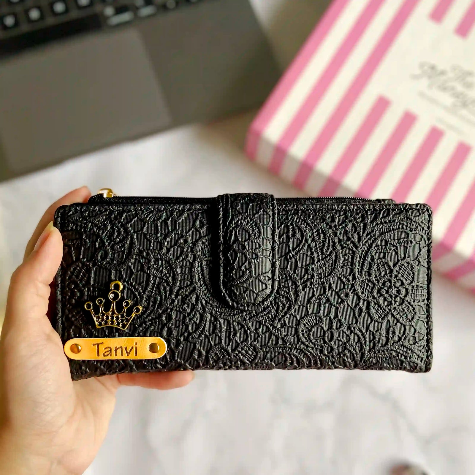Black lace wallet with 'Tanvi' held by a hand, blurred background