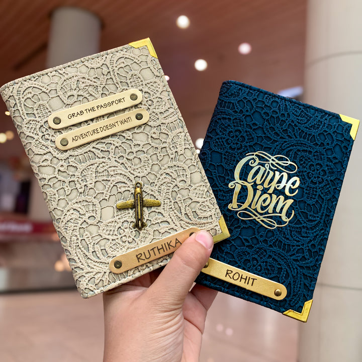 Two people holding black and white passport covers with custom text and charms, displayed in an airport setting.