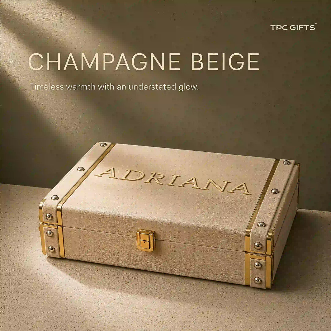 A champagne beige textured hard case with gold-toned metal corner protectors and a small gold clasp, embossed with the name &