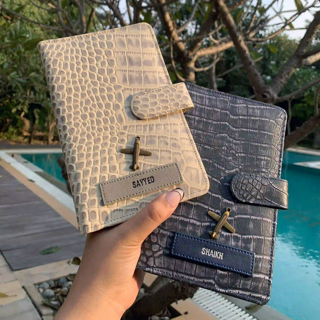 Two leather travel organizers held in hands, one in front and one in blue, displaying crocodile pattern, in taupe and blue colors - TPC Gifts