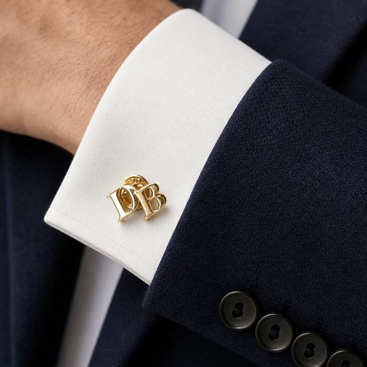Gold cufflinks with initials on a white cuff against a navy suit background