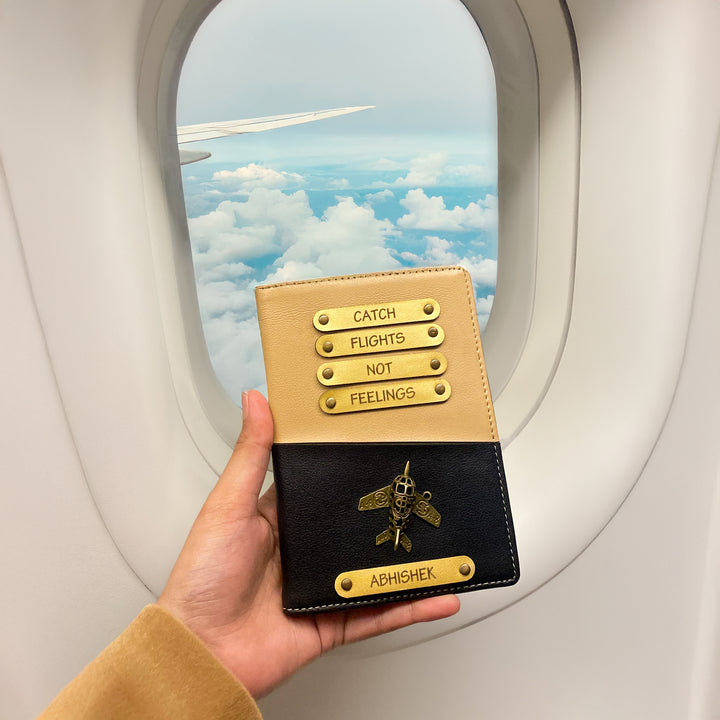 A person holding a dual tone black and beige passport cover with personalized text and a logo, while on an airplane with a cloudy sky outside the window.
