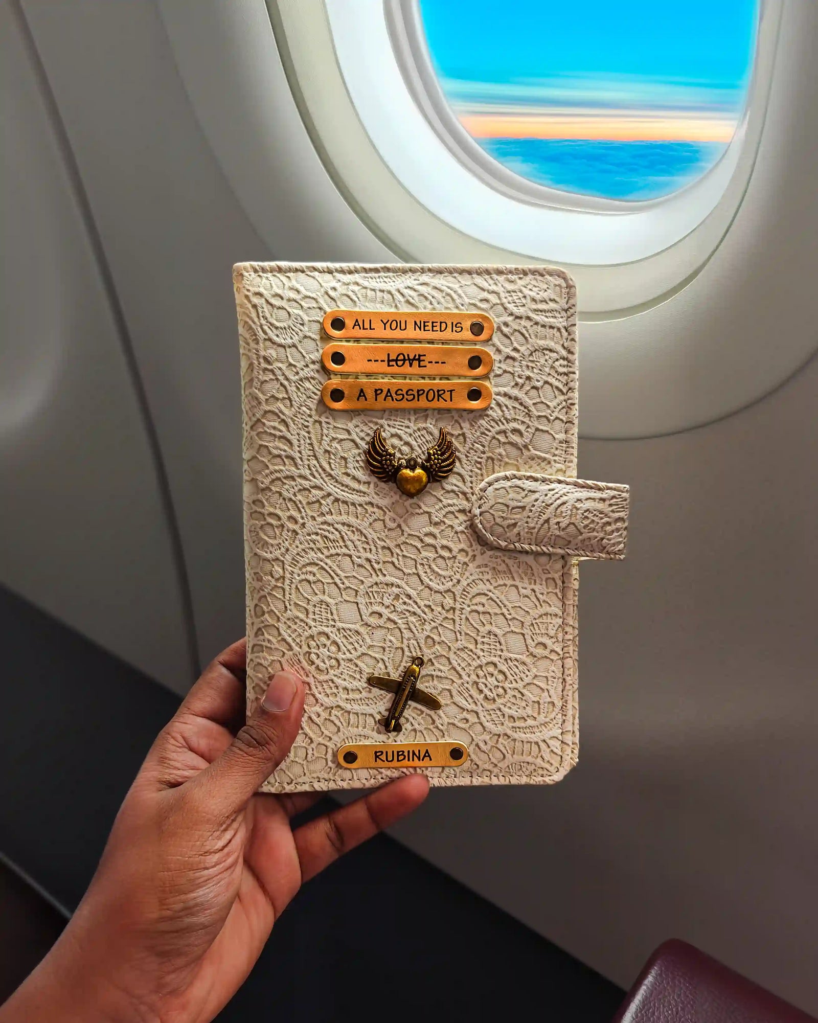 Hand holding a decorative travel wallet holder with airplane window in the background - TPC Gifts
