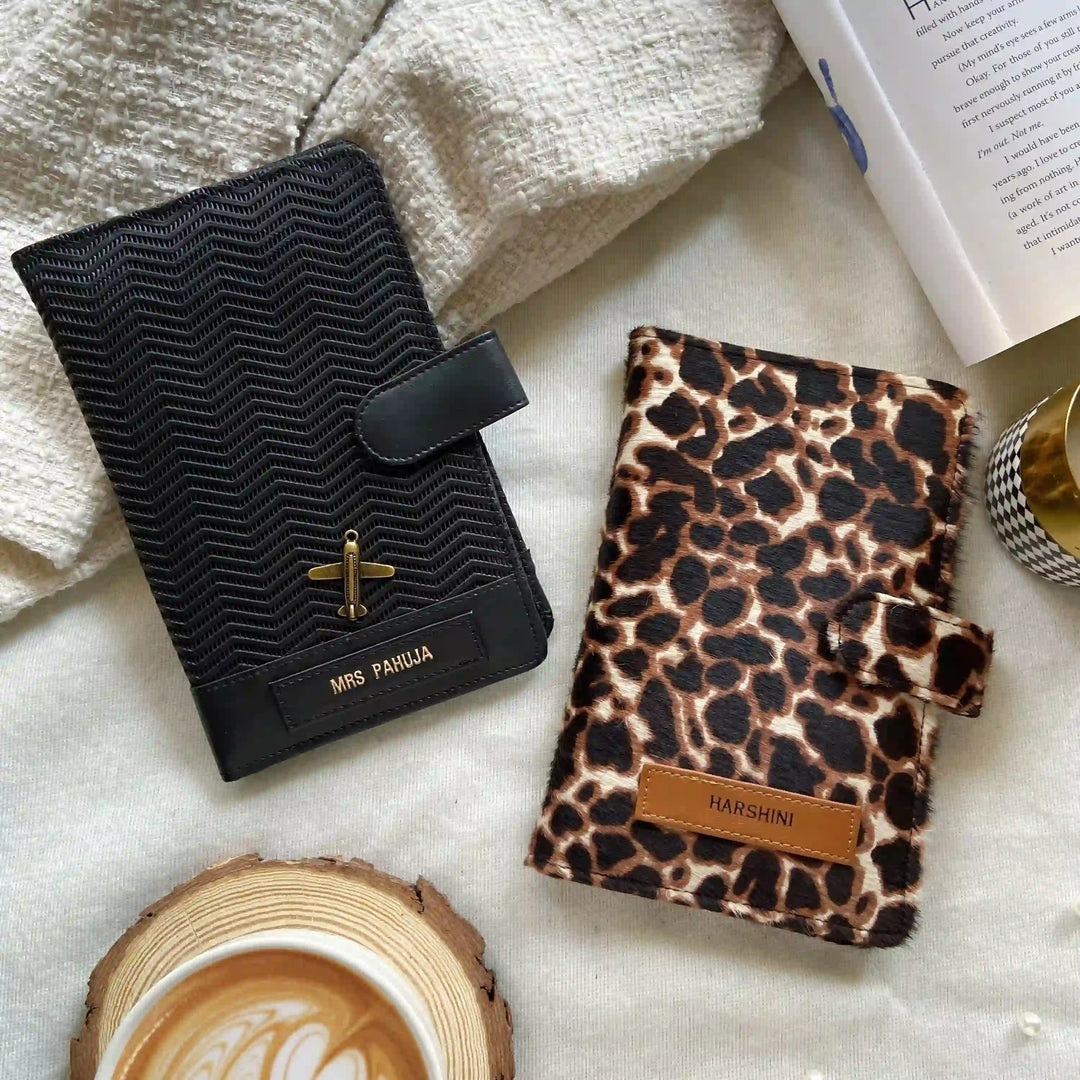 Two travel organizers, one with a black ziggy texture color and another with a animal print, placed on a surface with a cup of coffee and a book at backgroud setup from TPC Gifts