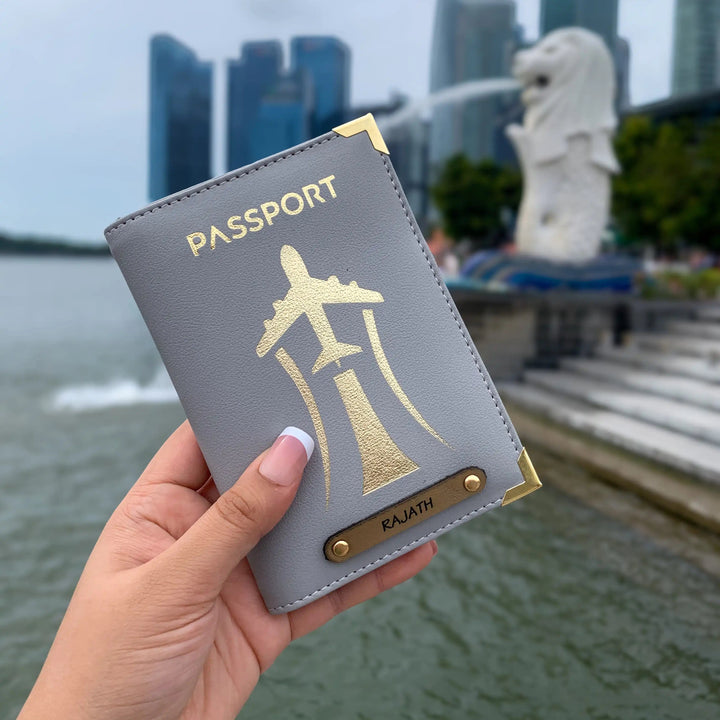 A hand holding a black passport cover with gold aviation-inspired design and text &