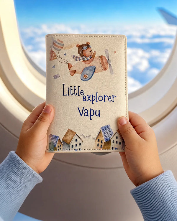 Children's passport wallet with airplane design and 'Little explorer Vapu' name, held against an airplane window background - TPC Gifts