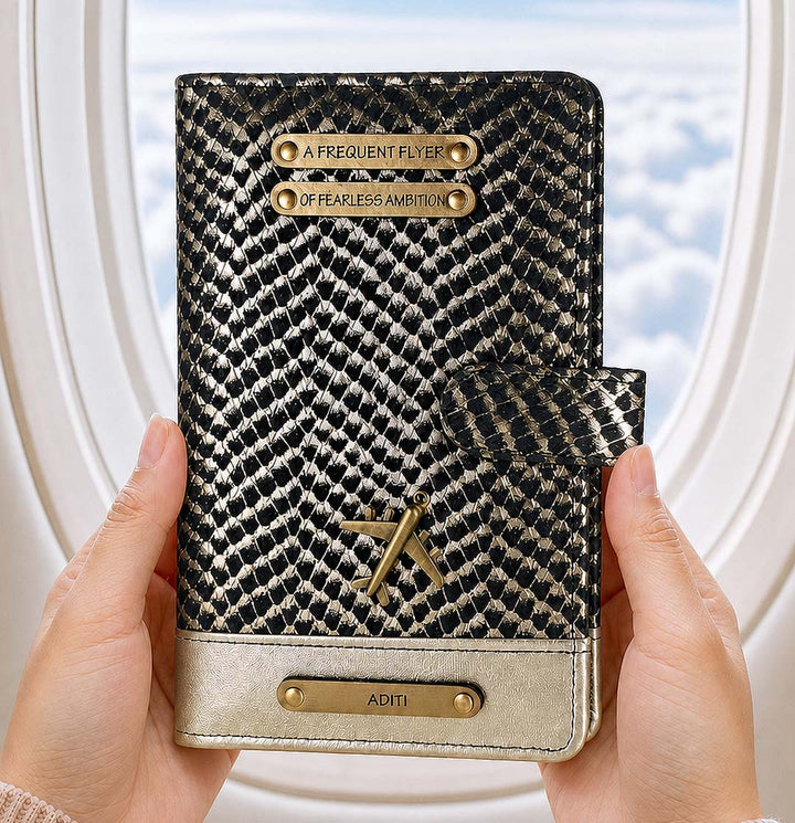 Patterned passport holder with gold accents held by hands against a blurred window background