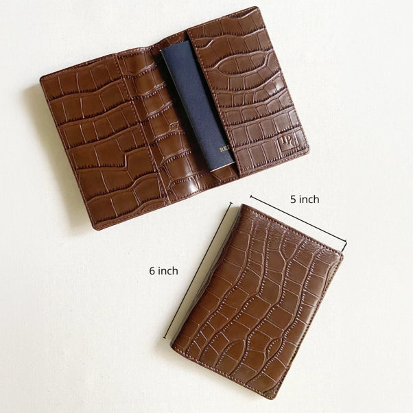 A brown crocodile-embossed leather passport holder shown open and closed on a light background, with dimension labels indicating 5 inch width and 6 inch height.