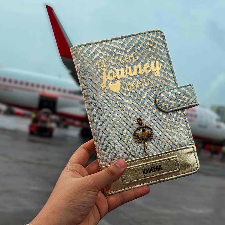 A personalized travel wallet by TPC Gifts with gold and ivory colors, featuring text and a crest design, held in a person&