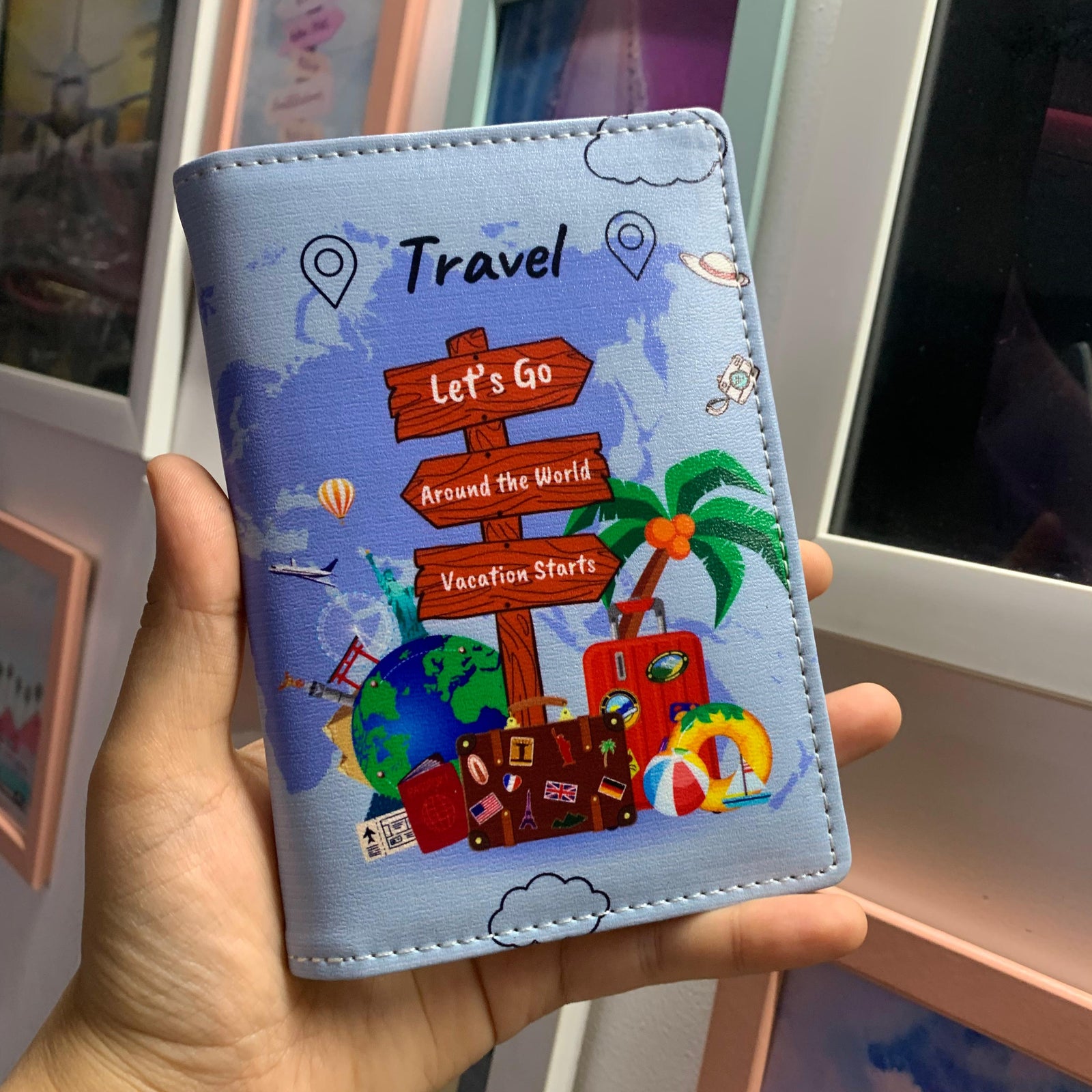 A hand holding a blue passport cover with a travel-themed print, including a map and the text 'TRAVEL'.