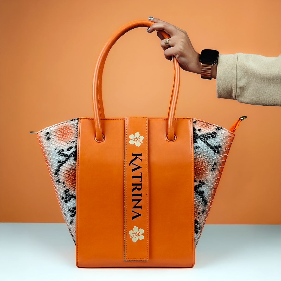 Orange handbag with 'Katrina' branding held by a hand against an orange background by TPC Gifts