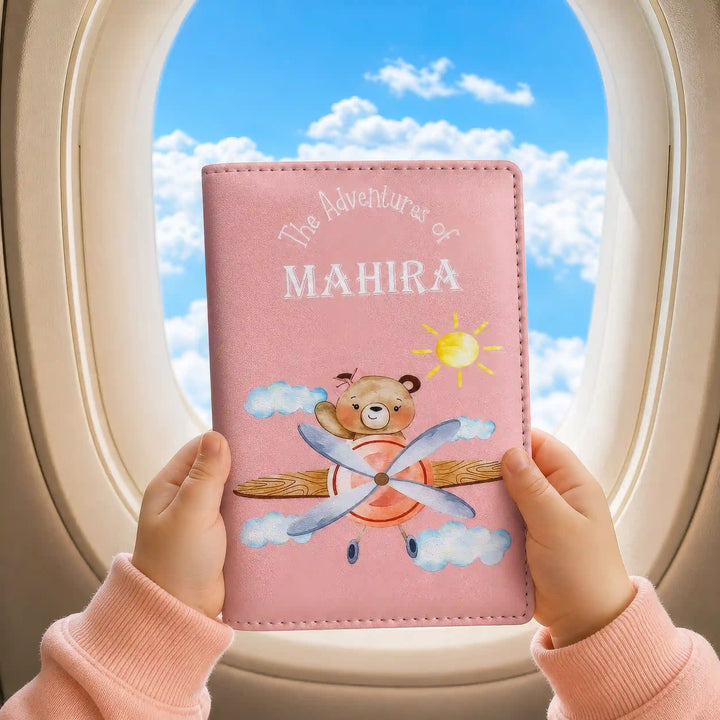 Pink travel journal with cartoon bear design held by a child against an airplane window view - TPC Gifts