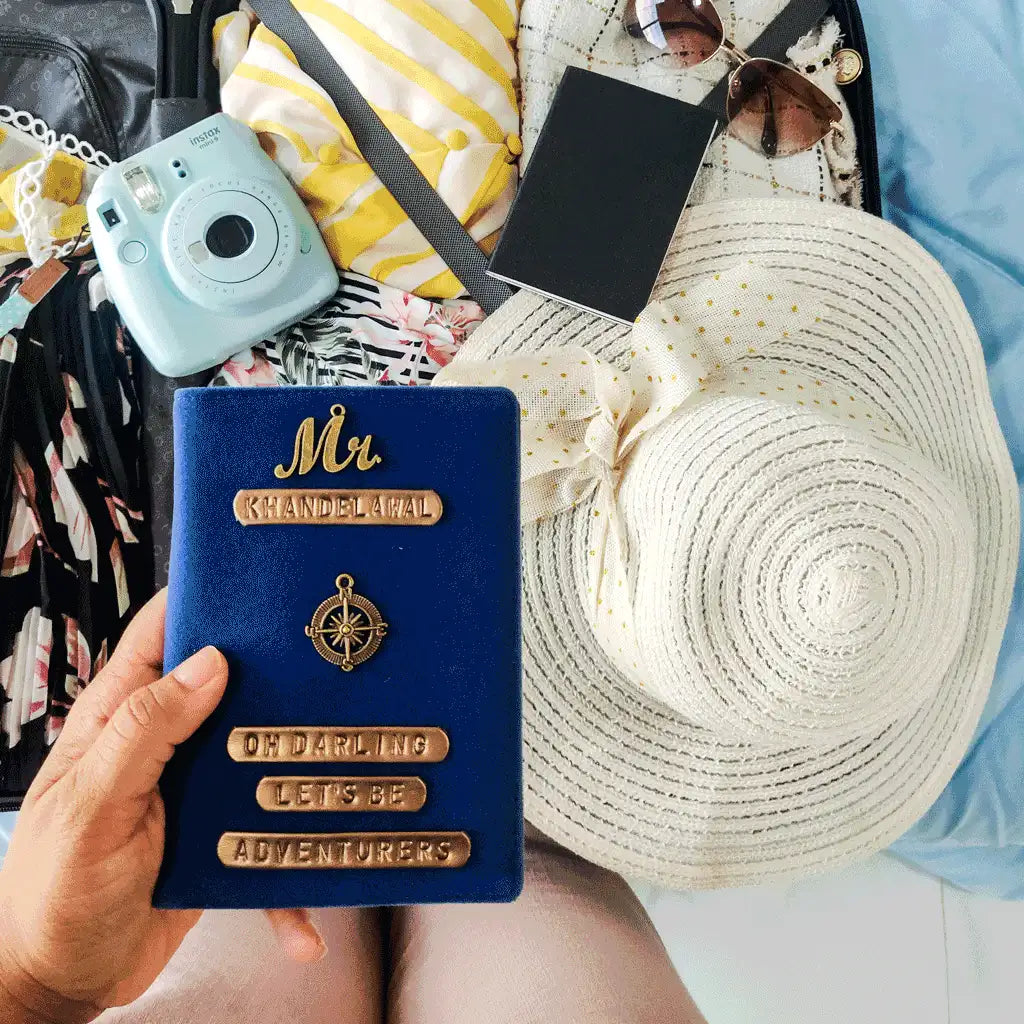 A hand holds a personalized blue velvet passport cover with gold lettering that reads &