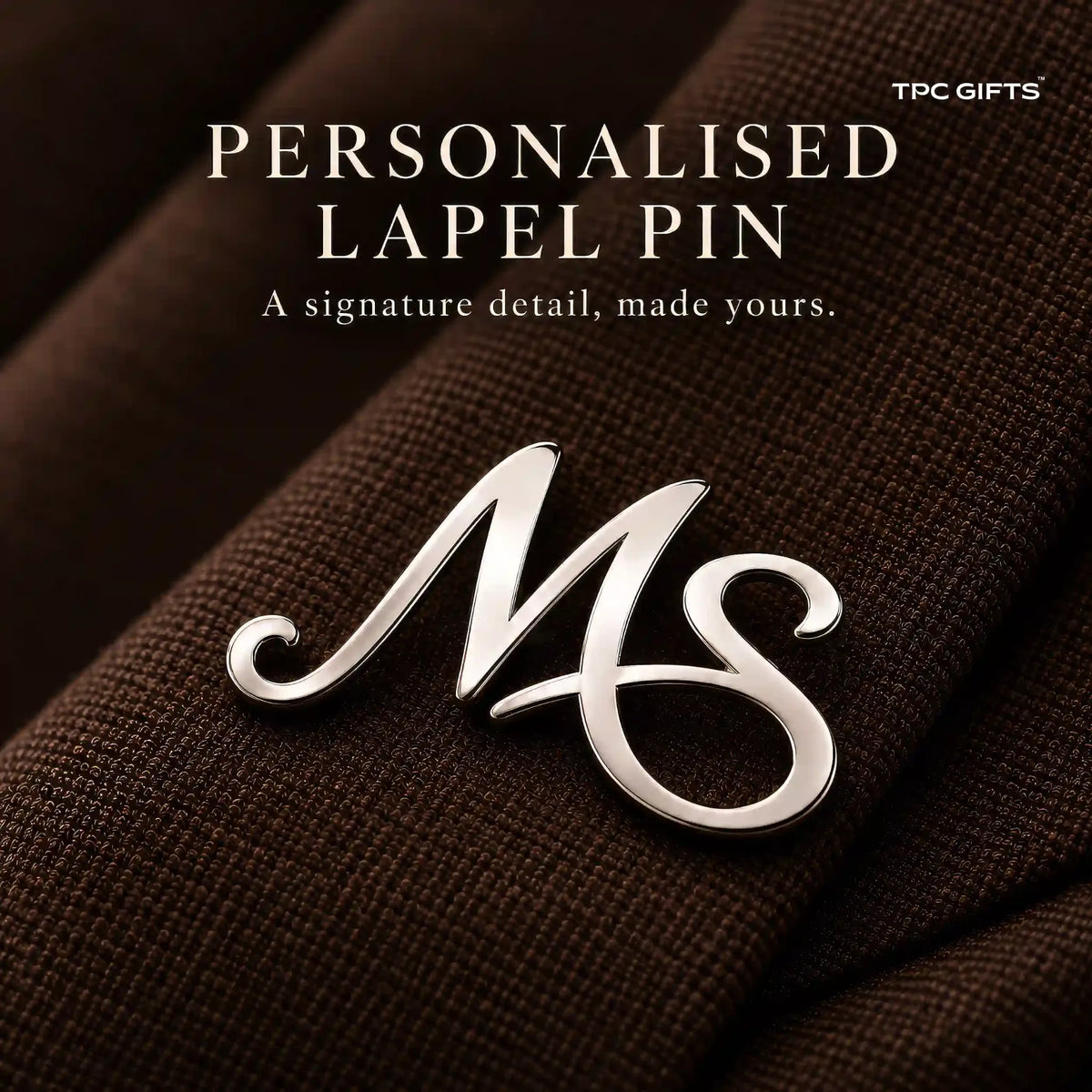 Personalised two initial silver tone lapel pin close up on brown fabric