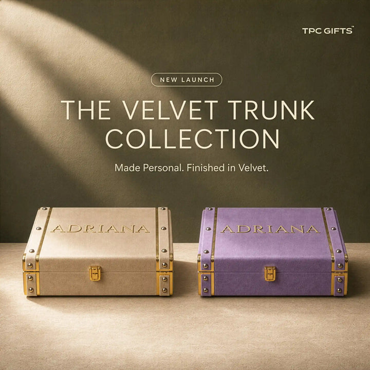 Two velvet trunk gift boxes labeled ADRIANA are shown side by side on a tabletop against a dark olive background with text reading &