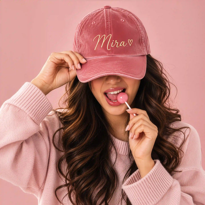Woman wearing a pink velvet baseball cap with the name "Mira" and a heart embroidered in gold cursive thread