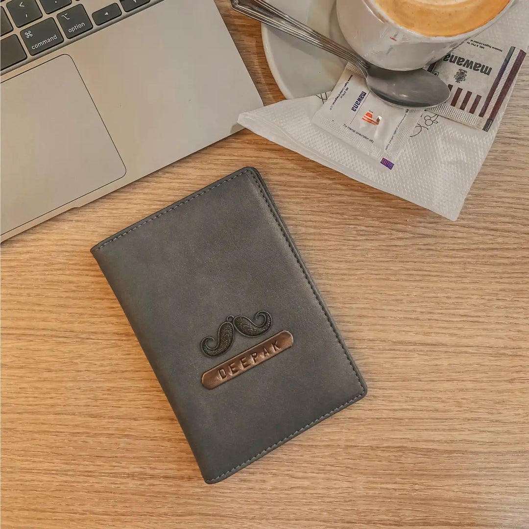 Personalised Grey Passport Cover with decorative emblem on a wooden table next to a laptop, coffee cup.Personalised Grey Passport Cover - TPC Gifts