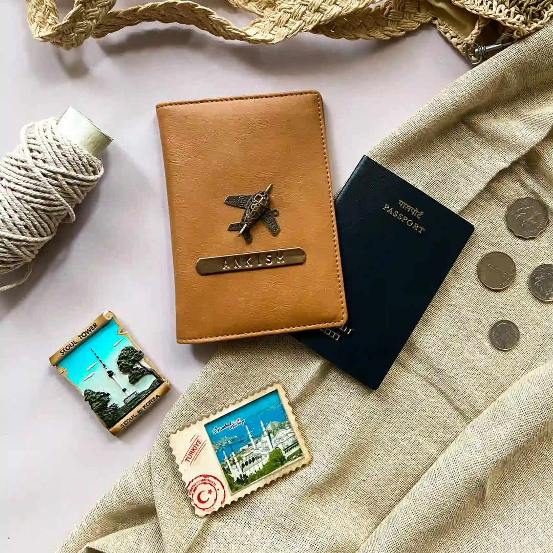 Personalised Tan Brown Passport Cover  with a plane emblem, black passport, and travel-themed cookies on a textured surface- TPC Gifts