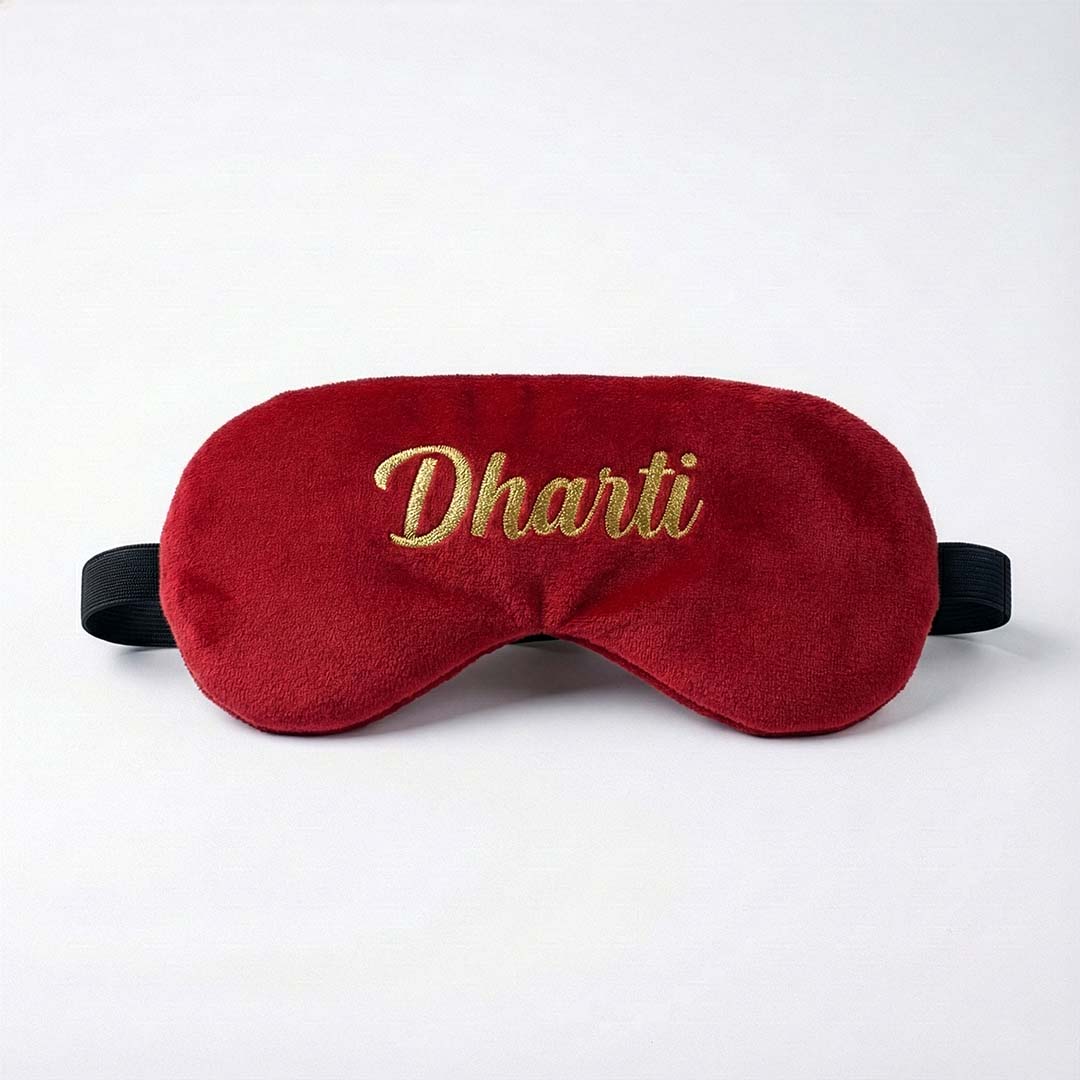Red travel sleep mask with 'Dharti' embroidery on a white background