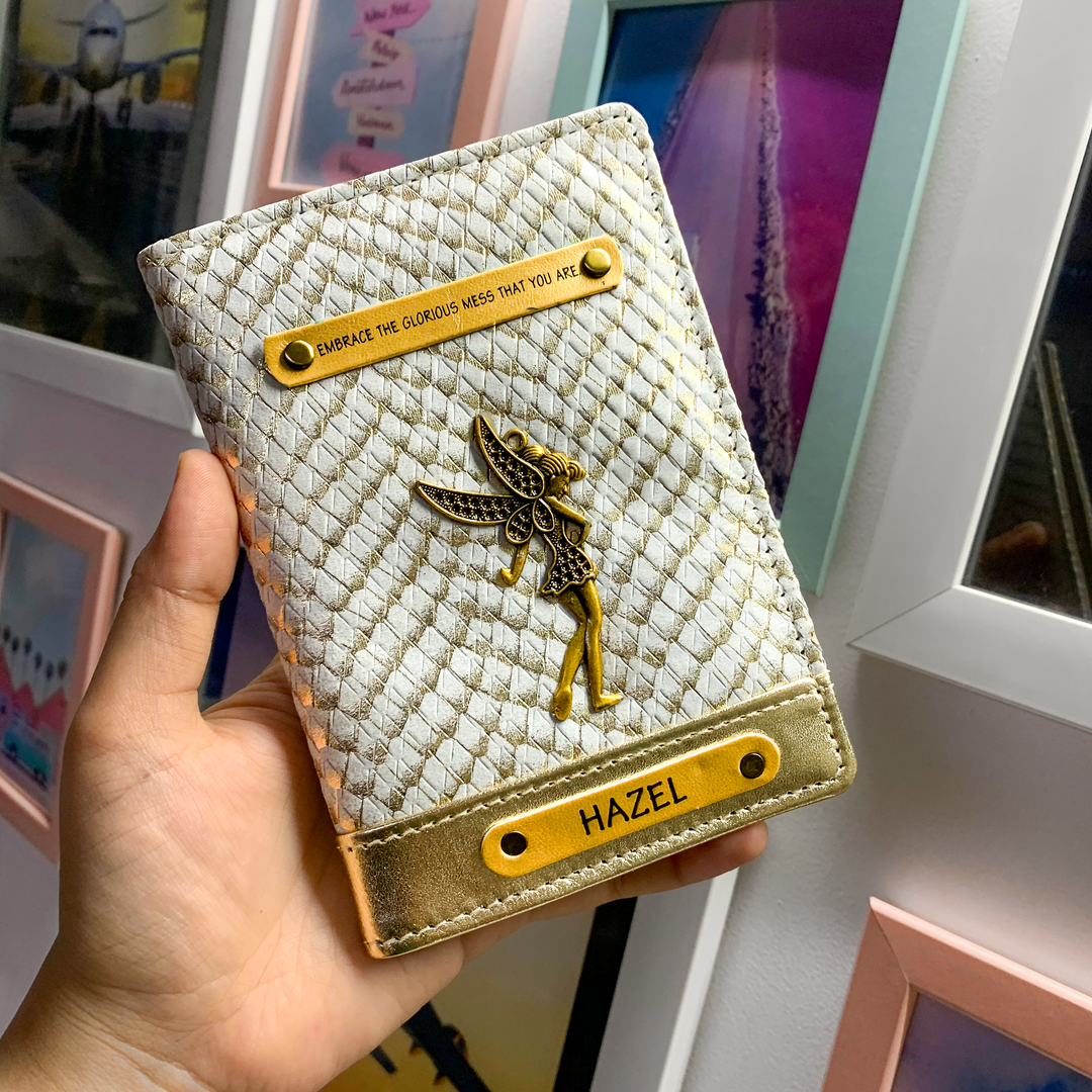 A personalized passport cover with a grape and gold color scheme, featuring a textured design and a gold-tone embossed emblem, held in a hand against a background of framed artwork.
