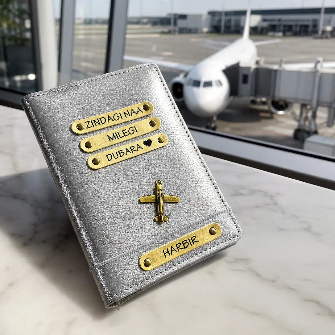 Silver passport holder with gold text and accents on a surface with an airplane in the background from tpc gifts