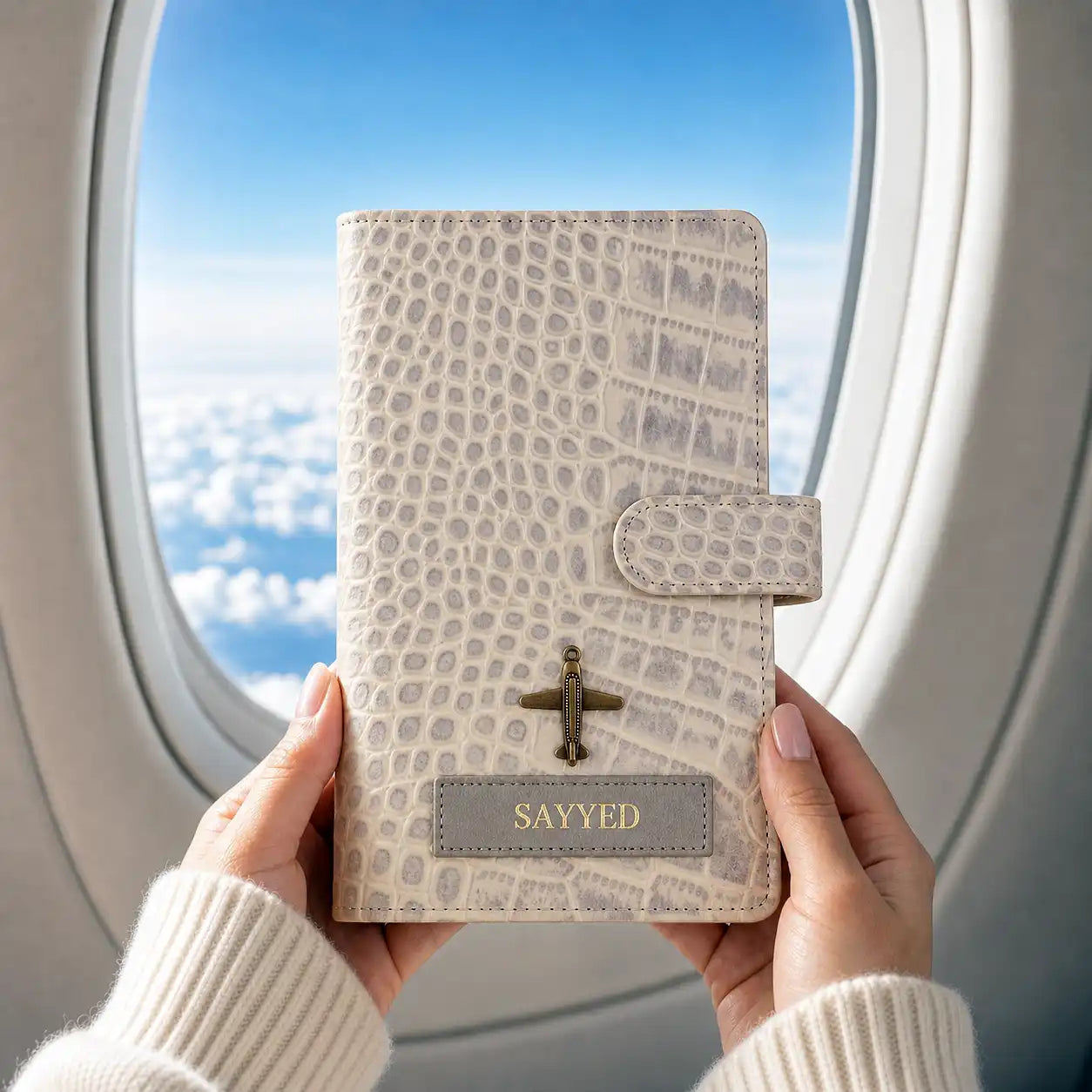 Personalised taupe croco texture genuine leather travel wallet in hand holding  with 'SAYYED' name and a charm on it in front of an airplane window- TPC Gifts