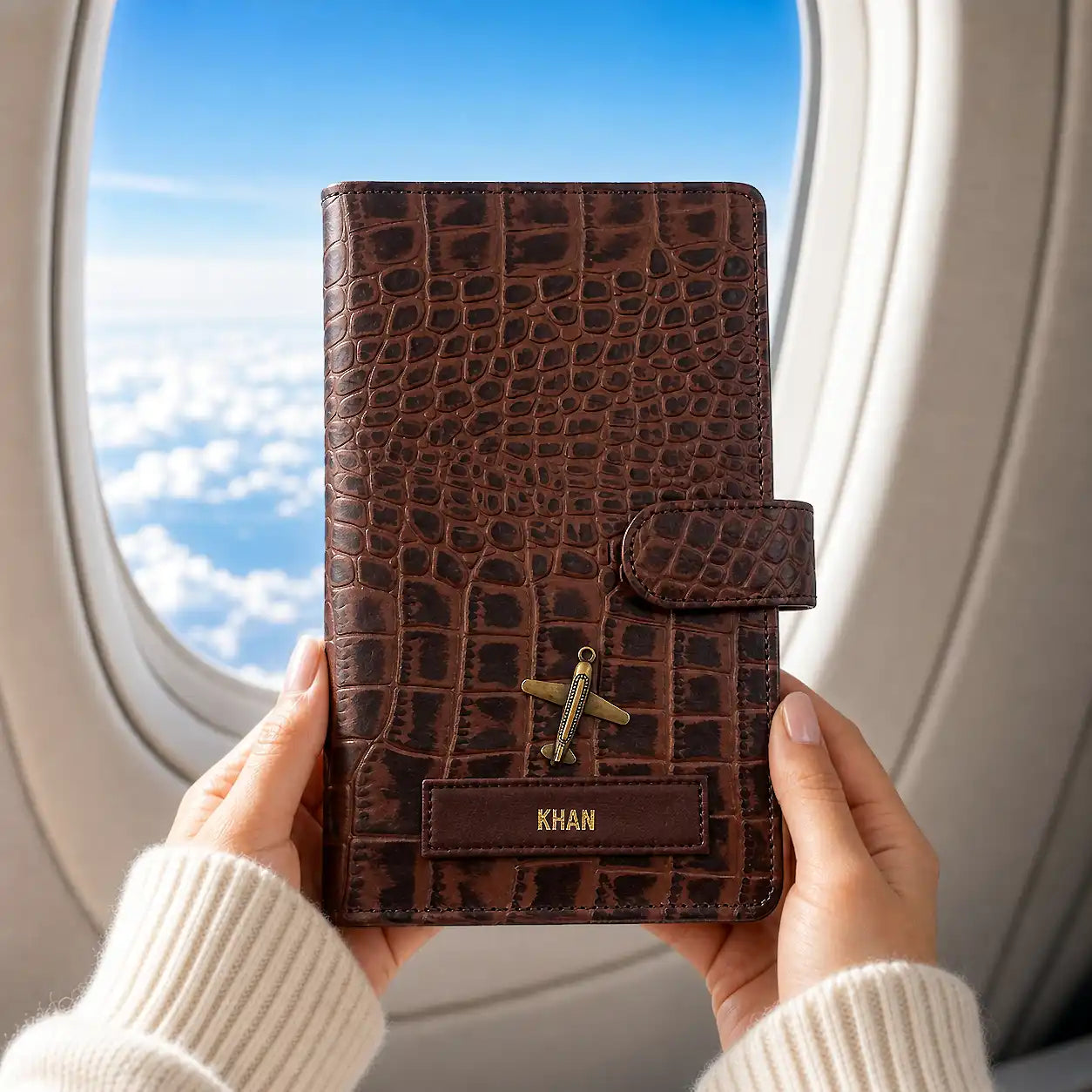 Brown crocodile-patterned genuine leather travel wallet held by hands with airplane window in background- TPC Gifts