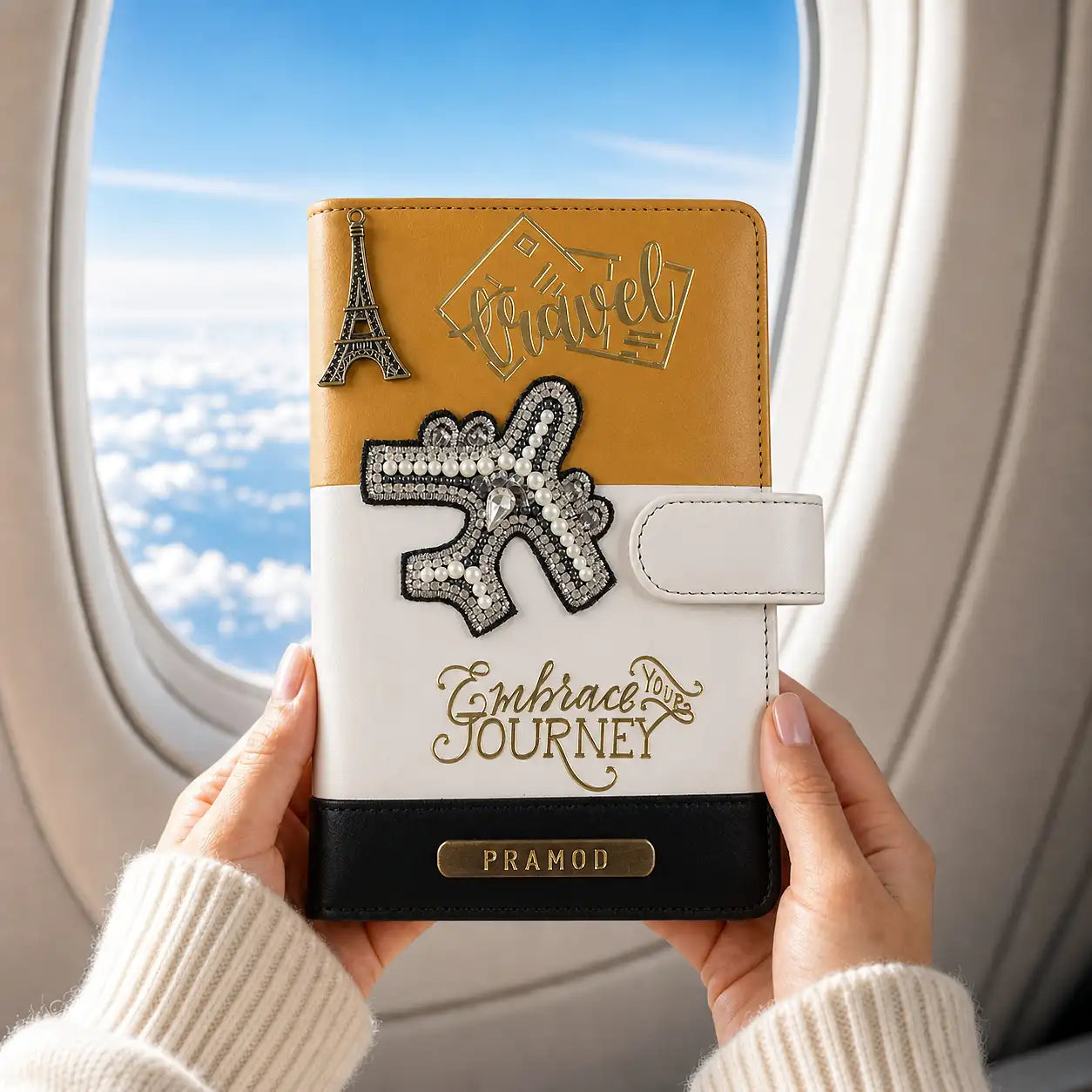 Person holding a personalized travel journal with decorative elements and airplane window in the background - TPC Gifts