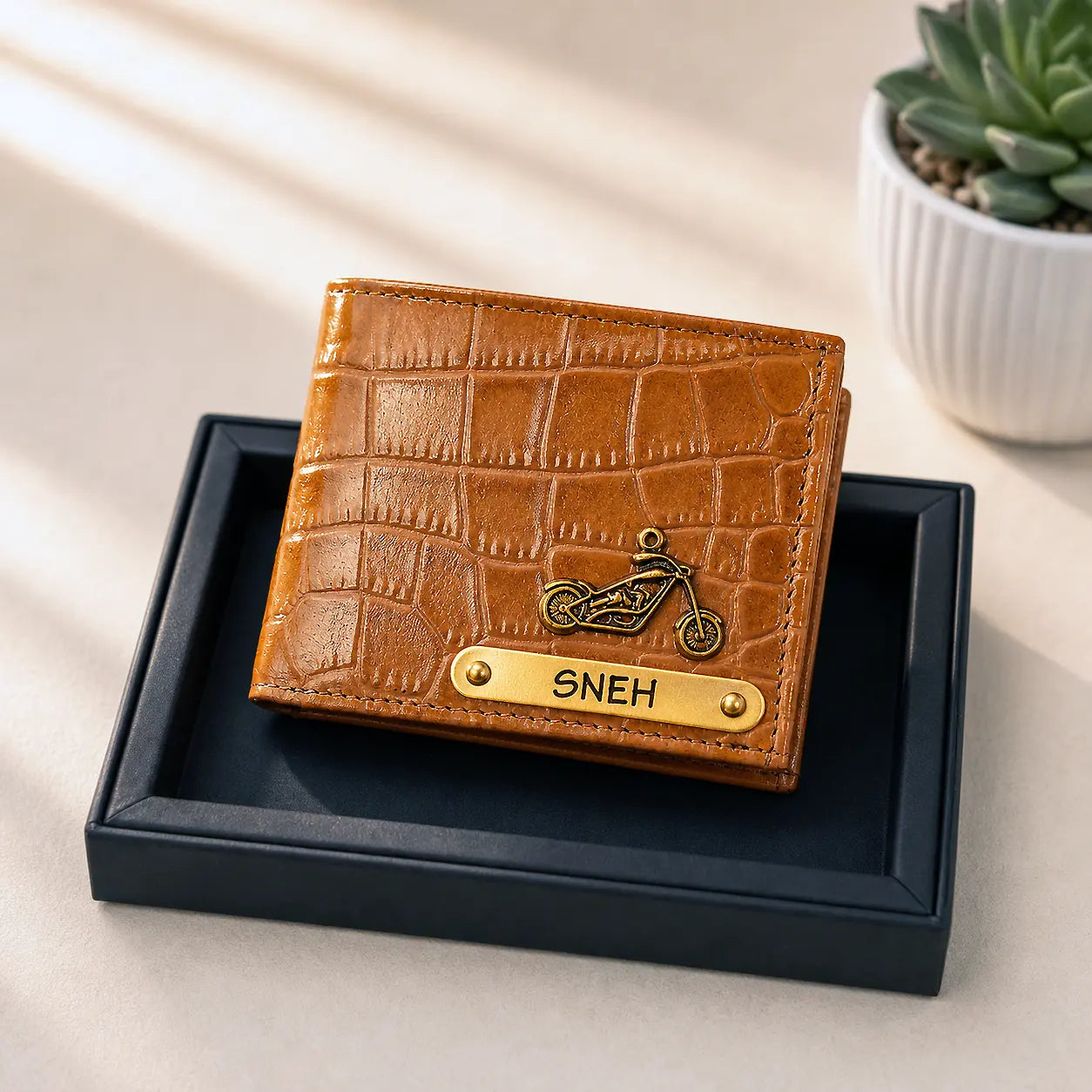 Brown textured wallet with 'SNEH' engraving on a black box, plant in the background by tpc gifts personalized wallet for men