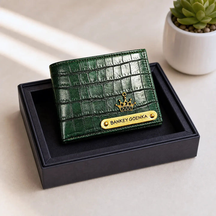 Green crocodile-patterned wallet with gold accents on a black box, featuring the name &