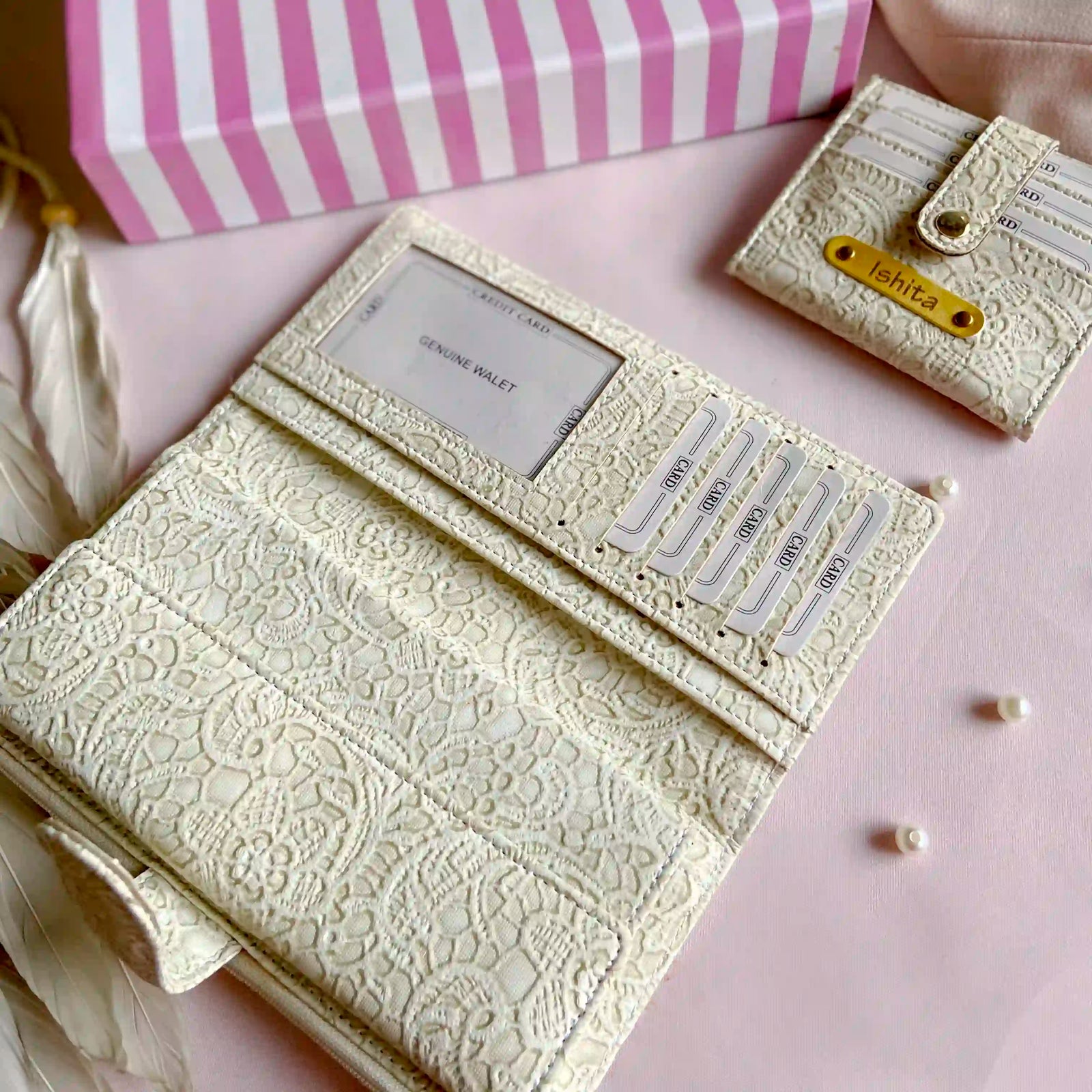Cream-colored lace wallet with a pink and white striped box on a pink surface.