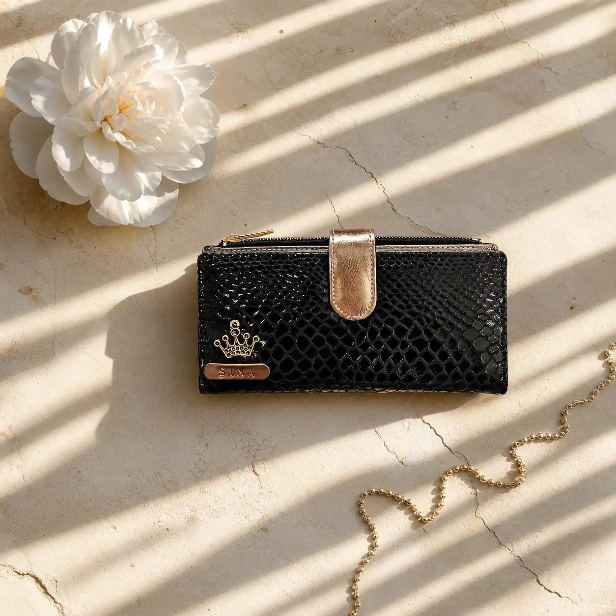 Black textured wallet with gold accents on a light surface with a white flowerby tpc gifts personalized wallet for women