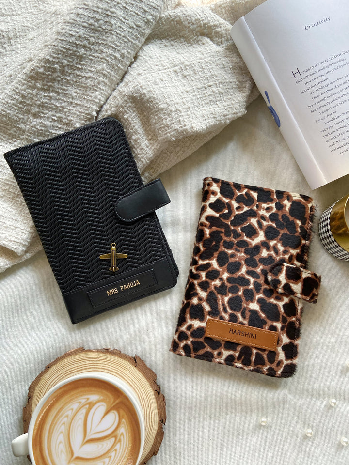 Two travel organizers, one with a black ziggy texture color and another with a animal print, placed on a surface with a cup of coffee and a book at backgroud setup from TPC Gifts