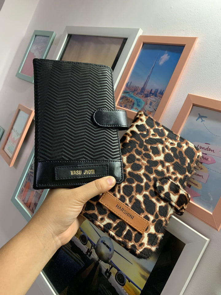 Two travel organizers, one with a black ziggy color and another with a animal print, placed on a surface with a cup of coffee and a book at backgroud setup from TPC Gifts