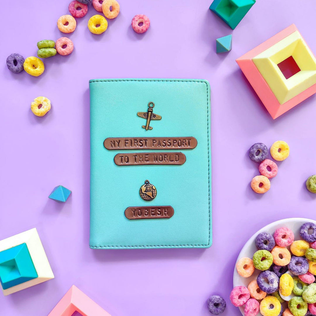 A pastel blue passport cover with a custom name tag and charm, displayed alongside colorful candy and geometric shapes on a purple background.